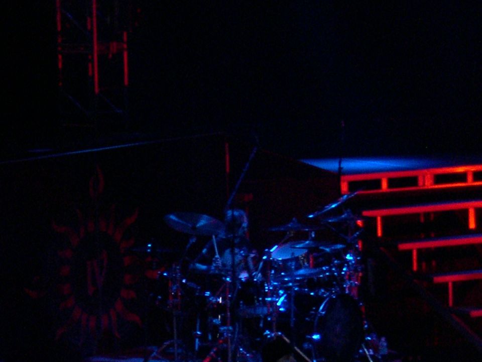 Drum set with cymbals and blue lights, on a dark stage with red lighting structure