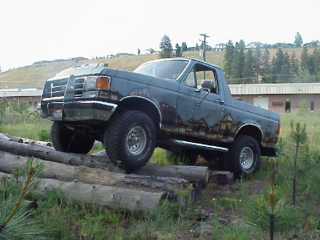 Dark blue Ford Bronco with a brush guard driving over logs
