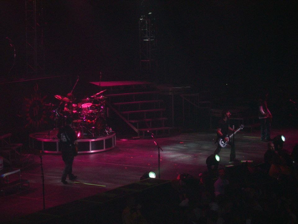 Stage with band members playing instruments and a drum kit under pink and white lights
