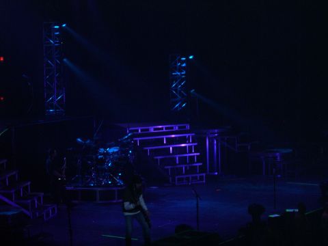 1997 Ford Probe - A concert stage is set up with lighting trusses, tiered stairs, and a drum kit, illuminated by blue lights.