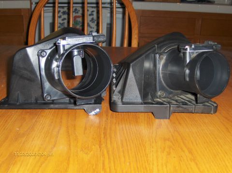 2004 Ford Crown Victoria - Two throttle bodies are shown on a wooden table, with a chair in the background.