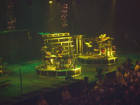 1997 Ford Probe - A concert stage is set up with two drum kits on raised platforms, illuminated by green and yellow lights.