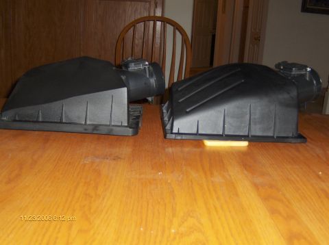 2004 Ford Crown Victoria - Two black plastic air intake boxes are shown on a wooden surface.