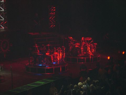 1997 Ford Probe - A concert stage is set with two drum kits under red lighting, with an audience watching.
