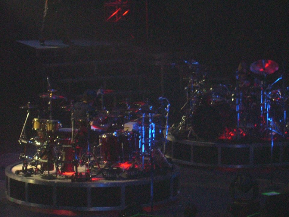 Two drum kits on circular stages with red and blue stage lighting