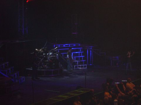 1997 Ford Probe - A band performs on a stage illuminated by blue lights, with a prominent drum set and stage scaffolding.