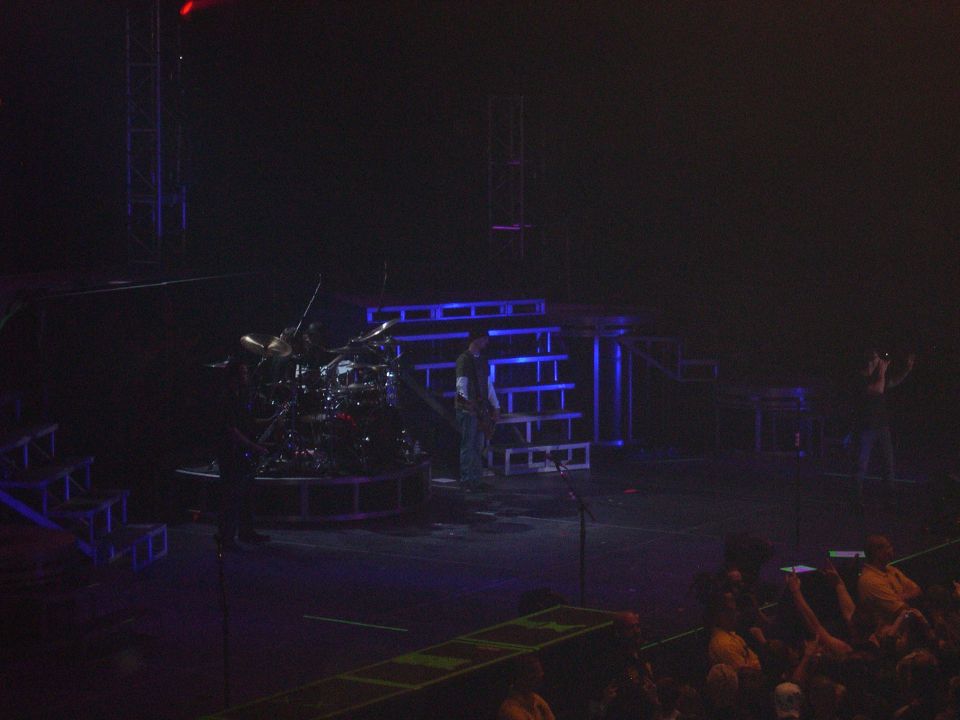 Stage setup with drum kit and band members performing, blue lighting