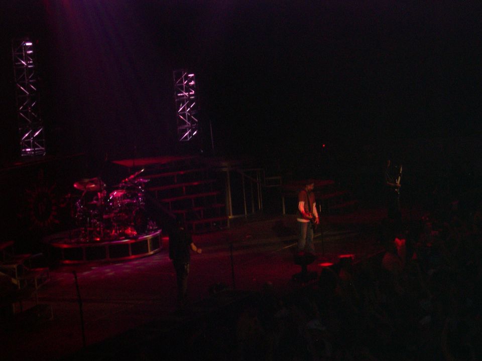 Concert stage with drum set and two people under purple and red lights