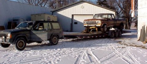 1979 Ford Bronco - A Jeep Cherokee sits in the snow next to a trailer loaded with a brown Ford pickup truck.