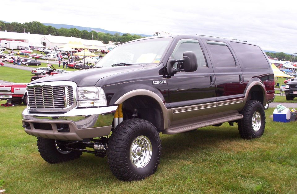Lifted dark brown 2000 Ford Excursion SUV with chrome wheels and off-road tires parked on grass