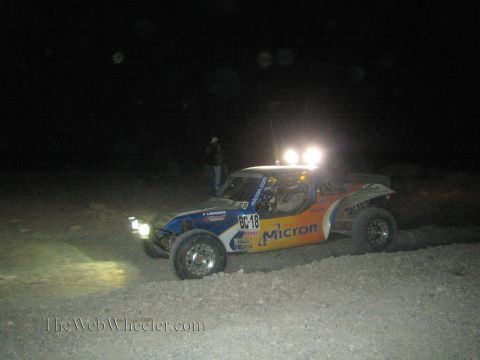 1990 Ford Bronco - orange and blue off-road race buggy with Micron sponsorship and a roof light bar races at night with a spectator watching.