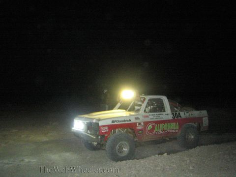 1990 Ford Bronco - red off-road race truck numbered 304 with BFGoodrich and California Tomatoes decals runs at night under a roof light bar.