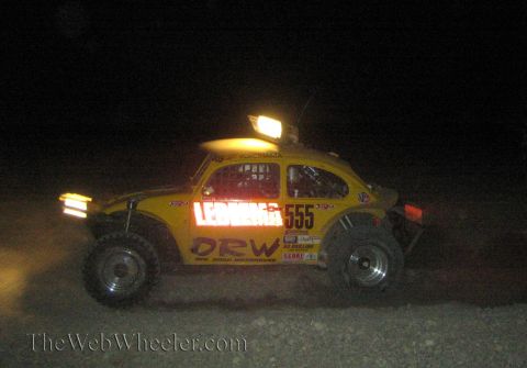 1990 Ford Bronco - yellow Volkswagen Beetle-based Baja race car numbered 555 with ORW decals races across the desert at night.