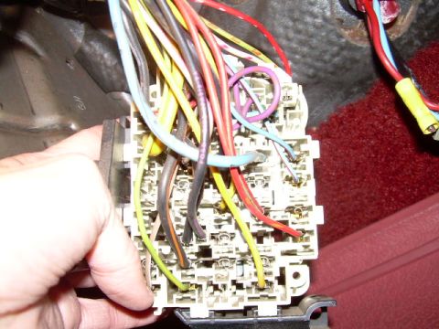1984 Ford Bronco - A hand is shown working on a complex fuse box with numerous wires.