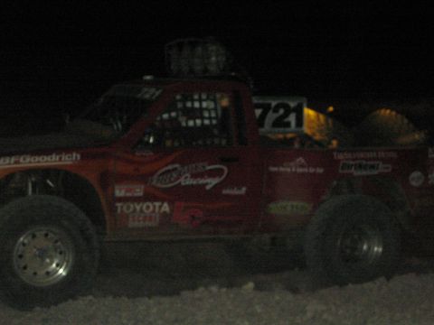 1990 Ford Bronco - red off-road race truck numbered 721 with BFGoodrich and Toyota decals and roof lights sits in the dark at night.