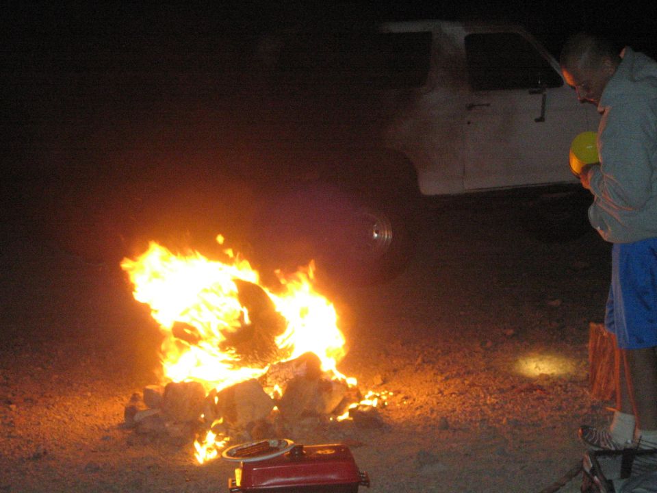 Campfire burning beside a white truck with a person standing nearby at night