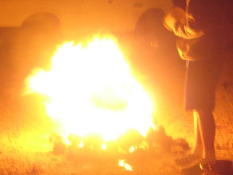 1990 Ford Bronco - bright blazing campfire lights up the desert ground as a person stands at the right edge of the frame at night.
