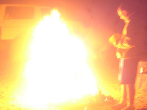 1990 Ford Bronco - tall blazing campfire glows brightly with a person standing at right and a pale van parked behind at night.