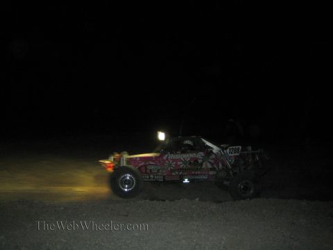 1990 Ford Bronco - off-road race buggy numbered 1206 with bright floral graphics runs through the dark desert at night.