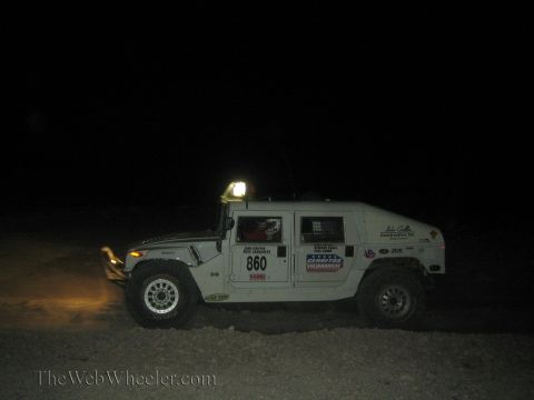1990 Ford Bronco - white Hummer H1 race vehicle numbered 860 with sponsor decals stands in the dark desert at night.