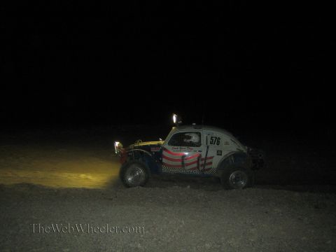 1990 Ford Bronco - Volkswagen Beetle-based Baja Bug race car numbered 576 with US-flag livery runs in the dark desert at night.