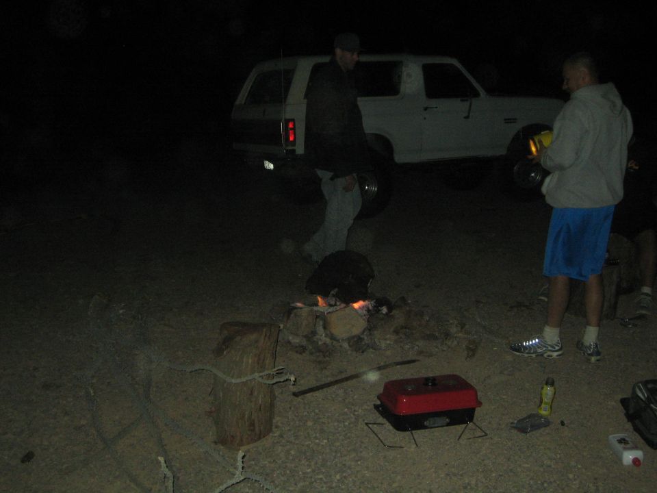 People around a campfire by a white SUV at night