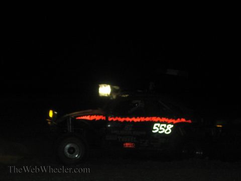 1990 Ford Bronco - off-road race car numbered 558 with red light trim and a roof light runs in the dark desert at night.
