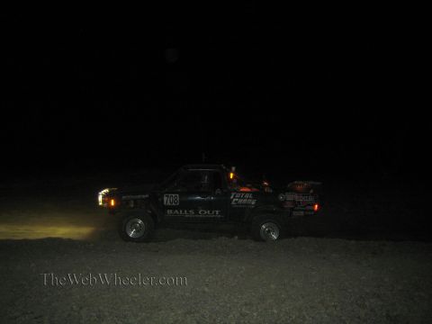 1990 Ford Bronco - black off-road race truck numbered 708 with Balls Out and Total Chaos decals races across the dark desert at night.