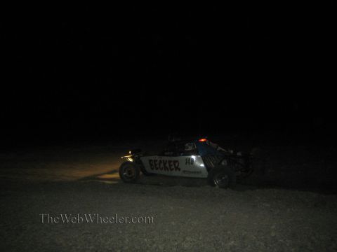 1990 Ford Bronco - off-road race buggy marked Becker number 140 drives across the dark desert lit by its headlights at night.