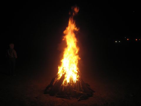 1990 Ford Bronco - tall bonfire burns brightly in the dark while a person stands at the left edge of the scene.