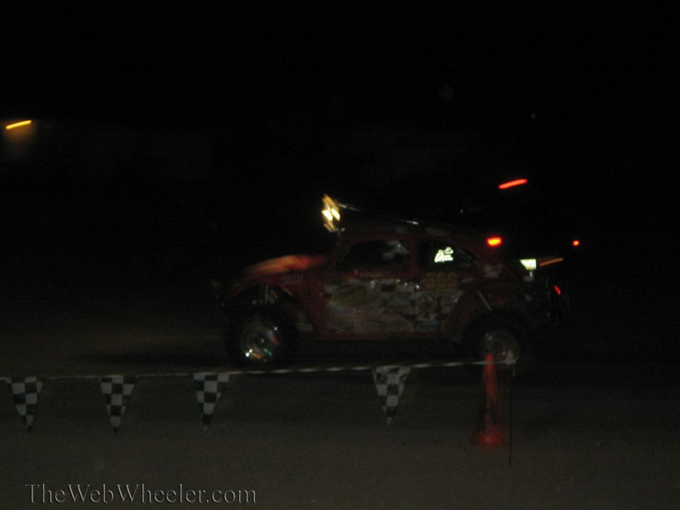 Red Baja Bug race car passing checkered barrier at night