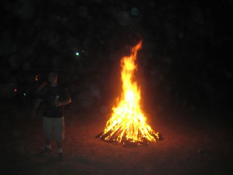 1990 Ford Bronco - man in shorts and a dark shirt stands beside a tall blazing bonfire in the dark at night.