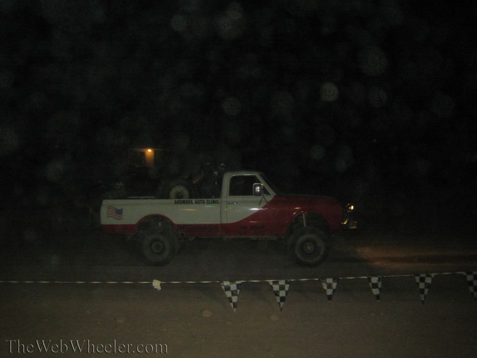 Red and white lifted pickup truck at night behind checkered race flags