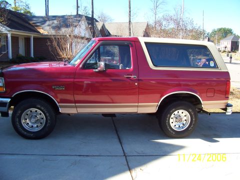 1994 Ford Bronco - A red and tan Ford Bronco SUV is parked on a concrete driveway in front of a house.