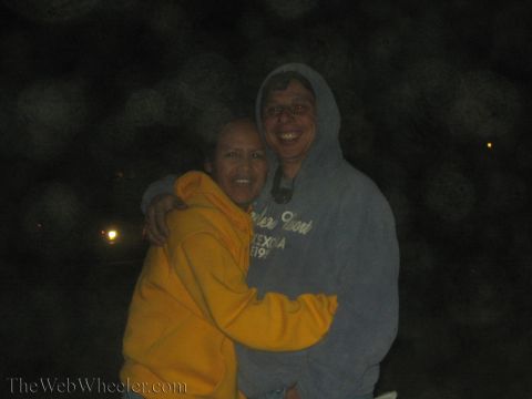 1990 Ford Bronco - woman in a yellow hoodie and a man in a gray hoodie smile and embrace for the camera in the dark.