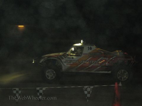 1990 Ford Bronco - red-and-white off-road race truck with 'GEOLANDAR' livery and number 14 sits behind checkered flags at night.