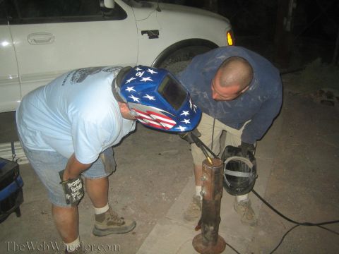 1990 Ford Bronco - Two men work on a rusty metal post at night, one wearing a stars-and-stripes welding helmet, beside a white truck.