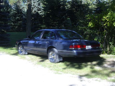 1996 Ford Crown Victoria - A dark blue sedan is parked on a grassy area with trees in the background.