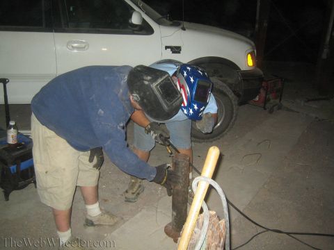 1990 Ford Bronco - man in a stars-and-stripes welding helmet bends over a rusty metal post at night near a white pickup truck.