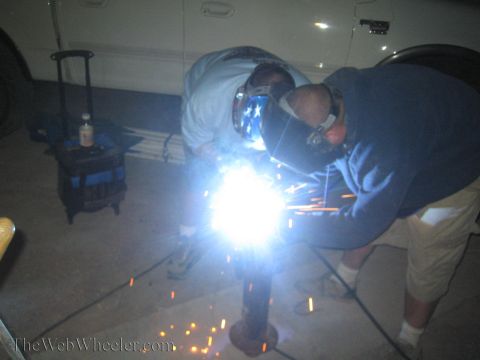 1990 Ford Bronco - Two masked welders lean over a vertical metal post throwing a bright shower of sparks in the dark.