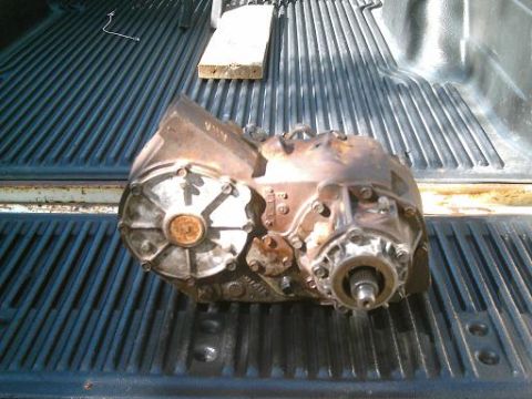 1986 Ford Bronco - A rusty transfer case is placed in the ribbed bed of a pickup truck.