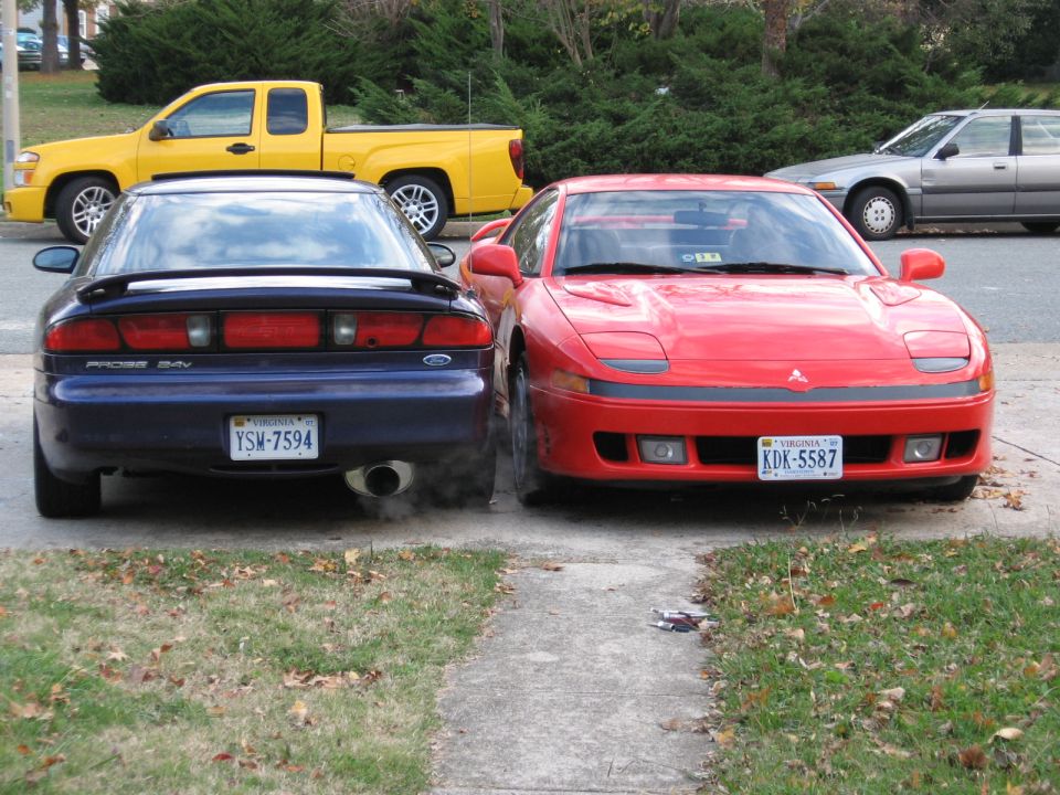 Red Mitsubishi 3000GT front view parked beside dark blue Ford Probe on a driveway