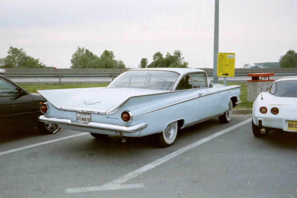Light blue 1959 Buick LeSabre parked in a lot, rear view. Whitewall tires and chrome bumper visible
