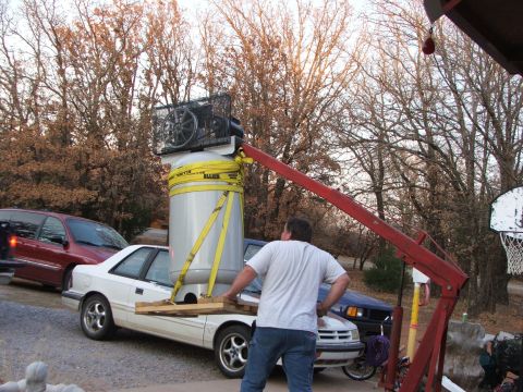 1965 Ford Mustang - Crane is lifting a large tank and air compressor onto a white sedan. Another vehicle is parked behind.