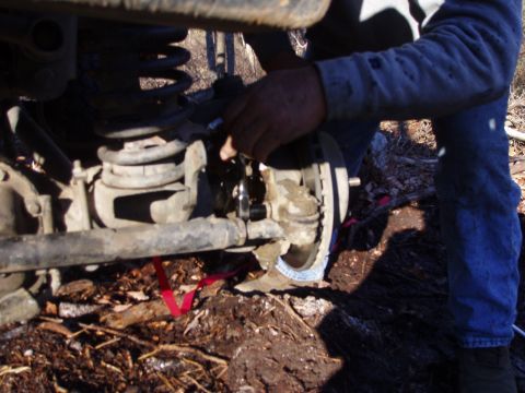 1989 Ford F-350 - A person works on the suspension and brake components of a vehicle, with the ground and debris visible below.