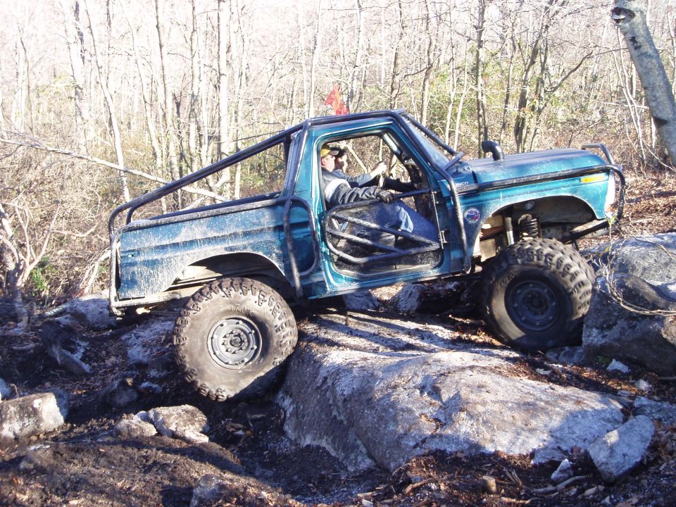 Teal off-road truck with roll cage and large tires climbing over rocks
