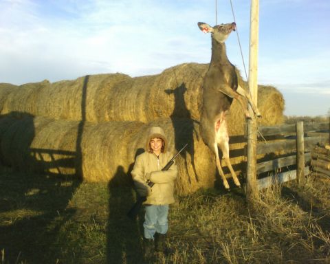 1989 Ford Bronco - A person stands with a rifle next to a deer hanging from a pole, with hay bales in the background.