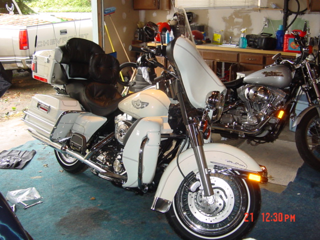 Two motorcycles parked in a garage, one white and one silver, with a white pickup truck visible in the background