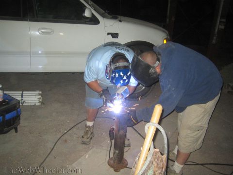 1990 Ford Bronco - Two men in welding masks lean over a rusty post throwing sparks at night, with a white pickup behind them.