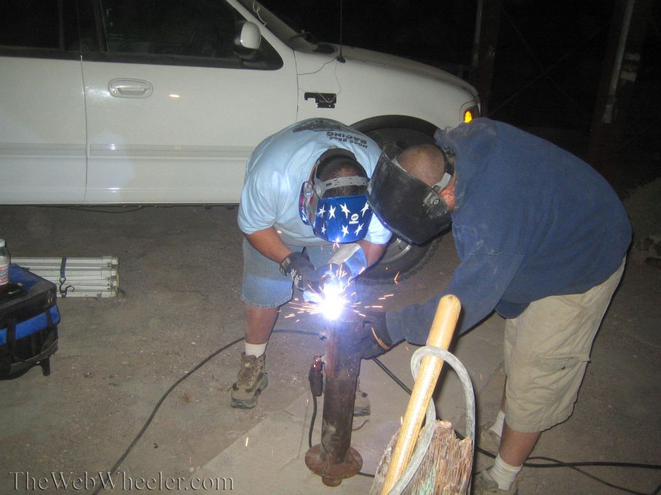 Two men welding a metal post at night beside a white pickup